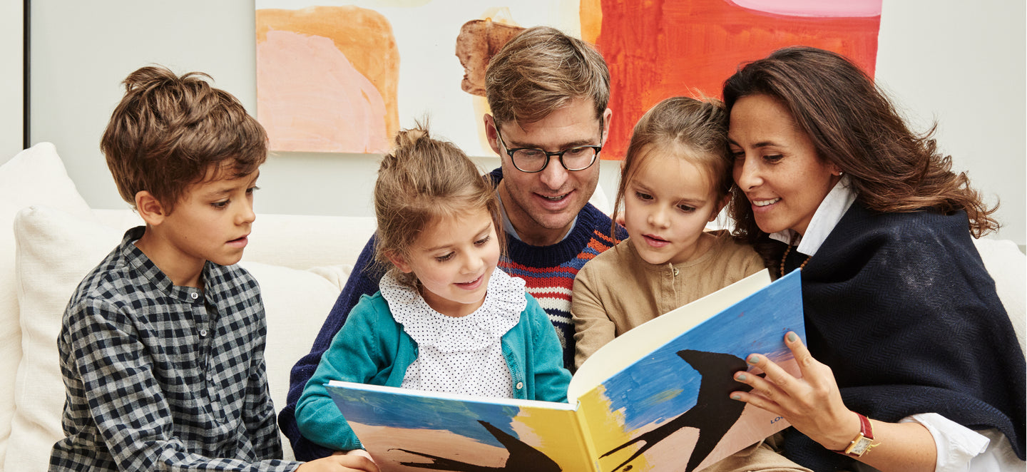 A family with young children gather round an open kids' art book