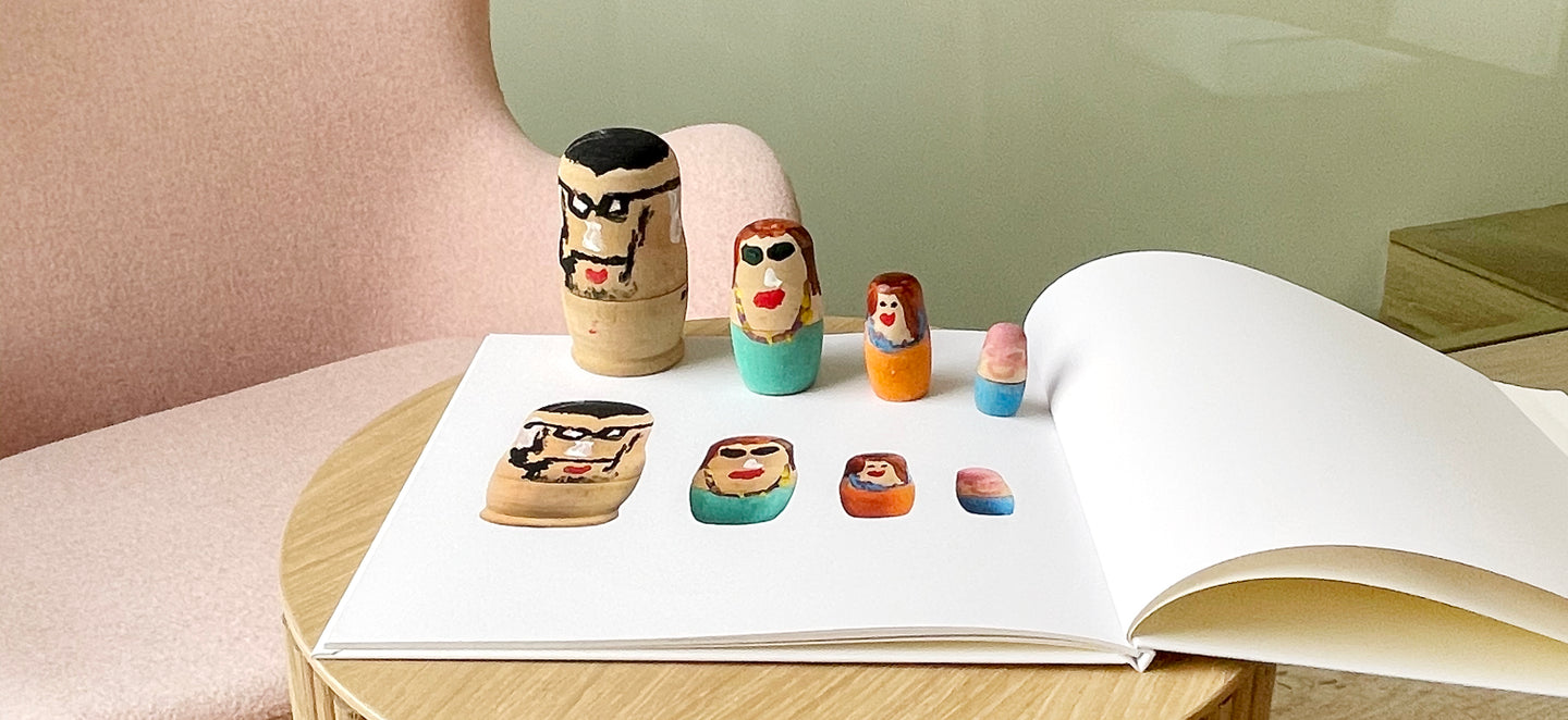 Russian dolls standing in a line on top of a book that has photos of the dolls printed on the page. The book is laying open on a coffee table