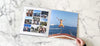 An open photo book on a marble table. The book spread has photos of a family on holiday including a child jumping into the sea from a boat.