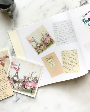 Open keepsake book on a marble coffee table showing old greeting cards printed on the pages including the messages written by friends and family members.