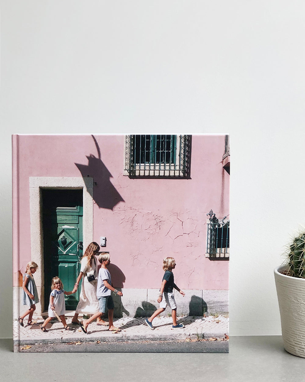 A photo book with a family on the front on holiday. The book stands next to a cactus on a shelf