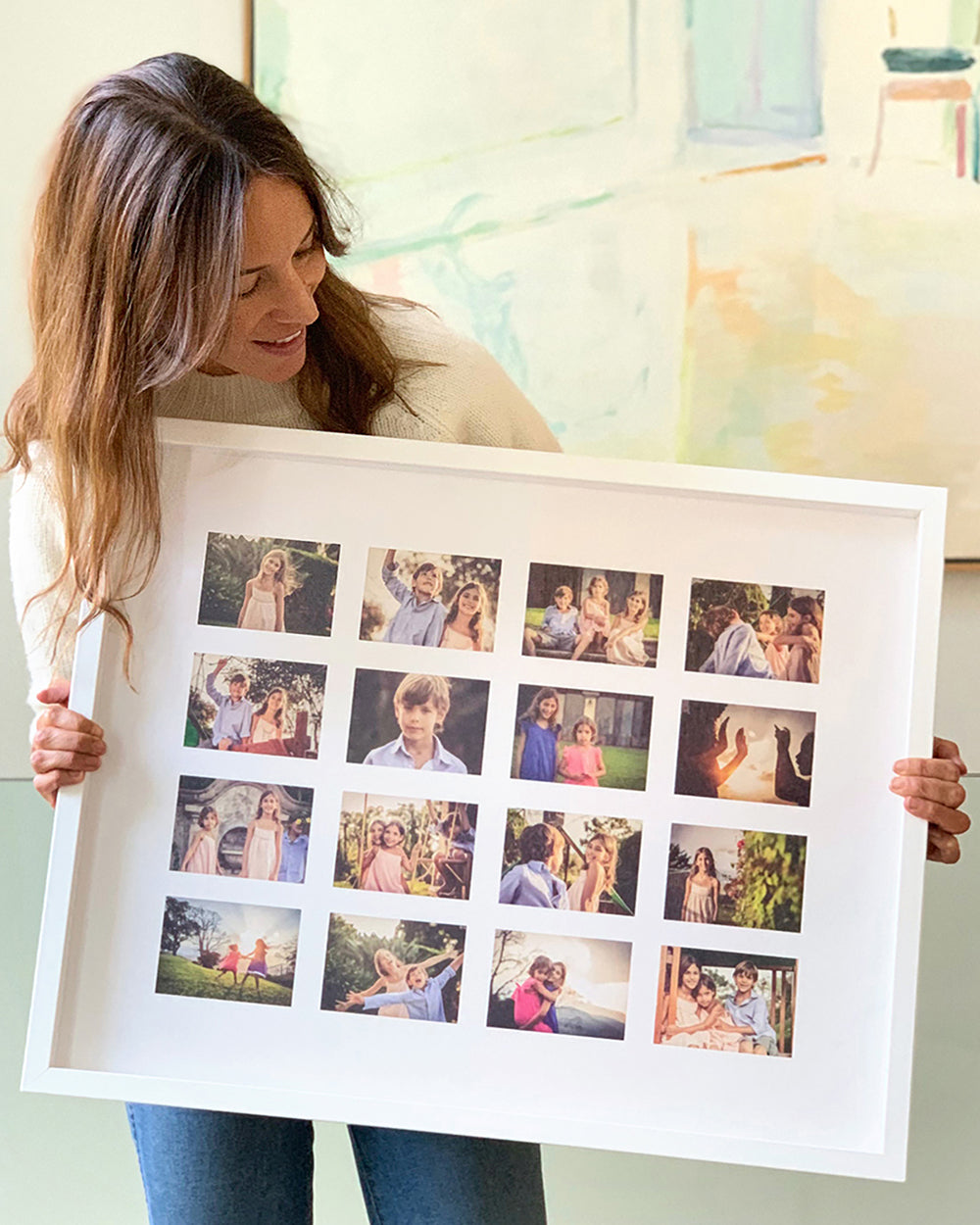 A woman holding a framed photo collage with multiple family photographs arranged in a grid pattern.