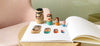 Russian dolls standing in a line on top of a book that has photos of the dolls printed on the page. The book is laying open on a coffee table