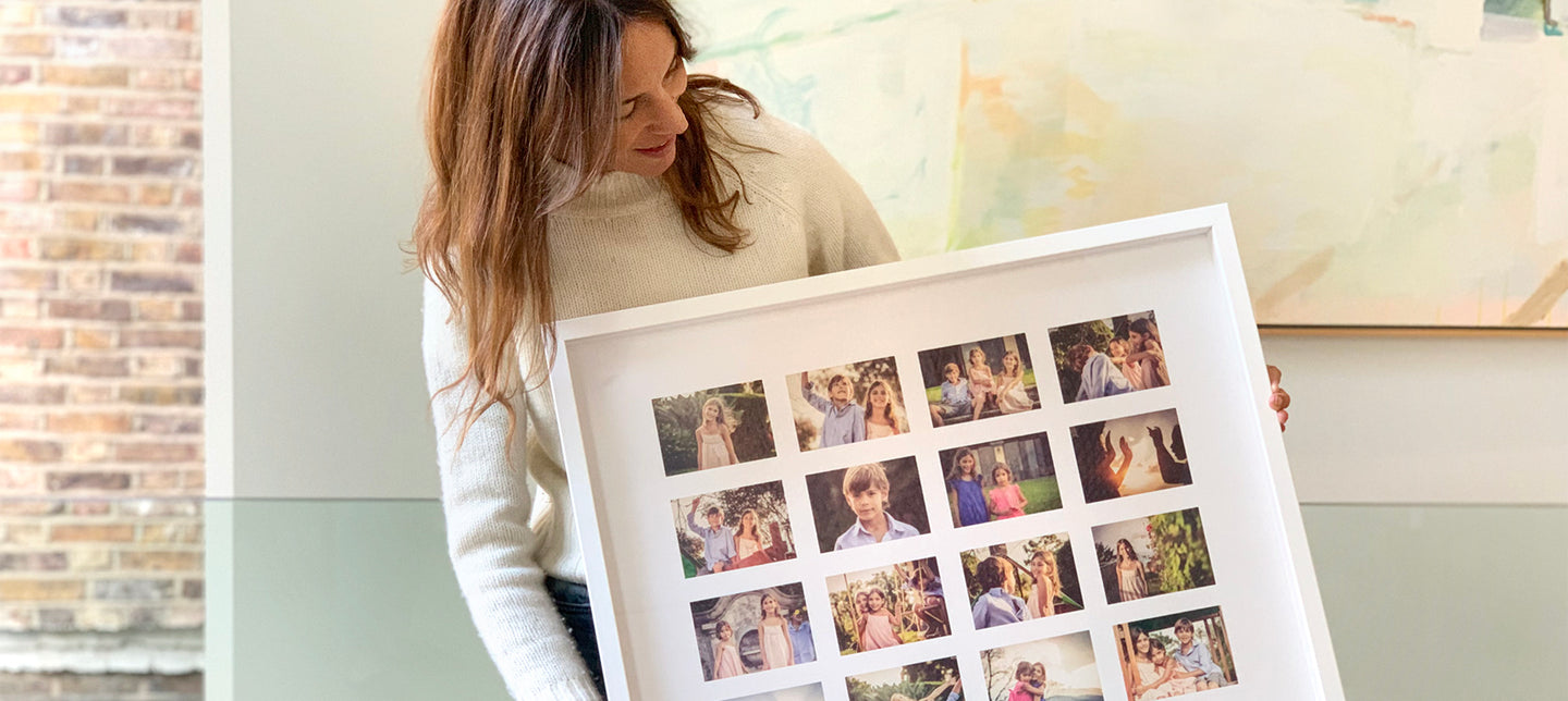 A woman holding a framed photo collage with multiple family photographs arranged in a grid pattern.